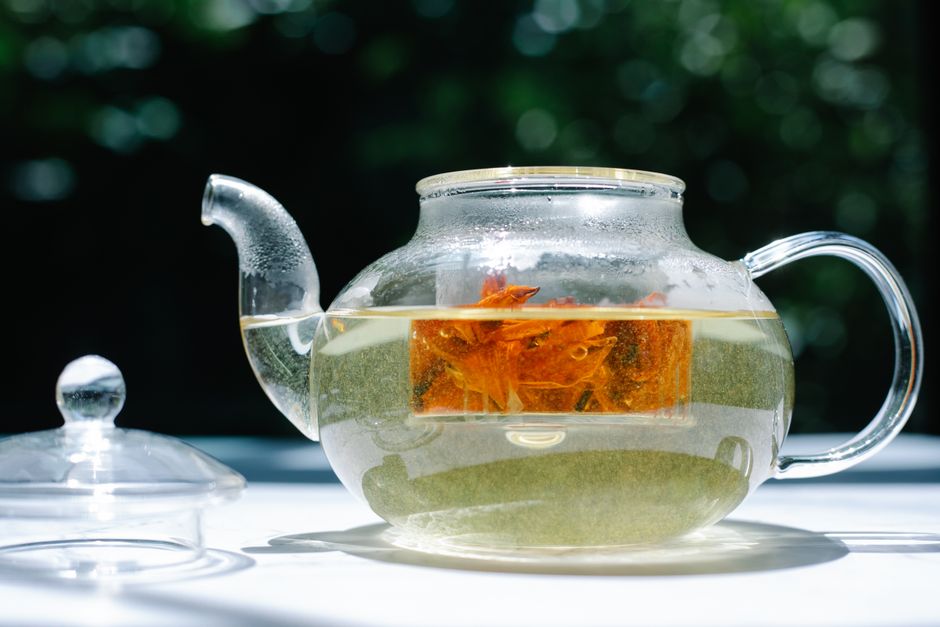 Glass teapot featuring a vibrant herbal tea infusion captured in bright sunlight, offering a refreshing view.