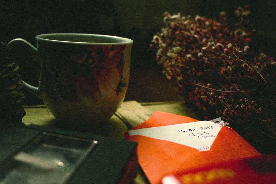 Ceramic cup with flower ornament placed on table with flowers and letter in bright envelope and videotape