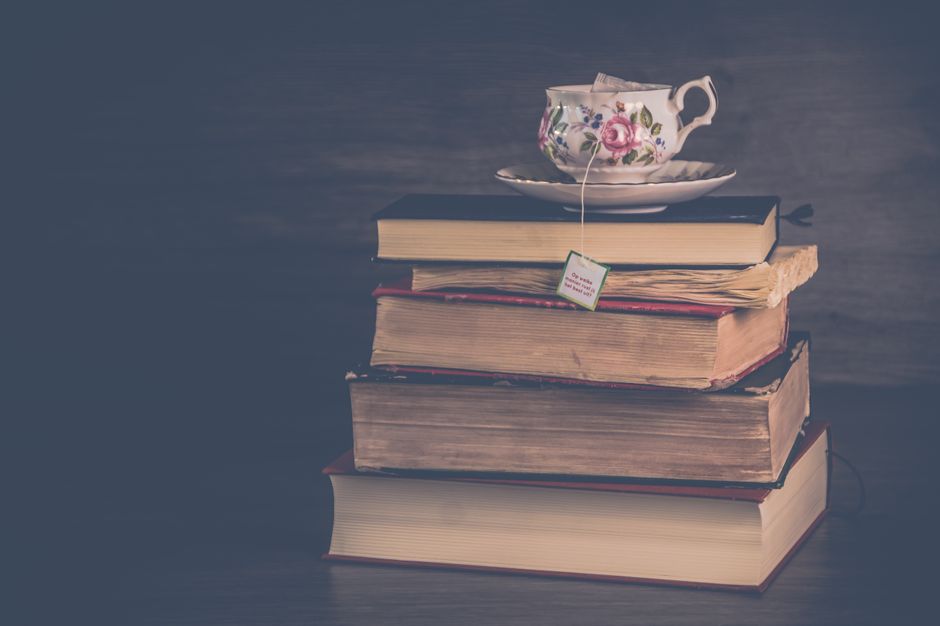 Elegant vintage teacup with floral design resting atop a pile of old books, evoking nostalgic charm.